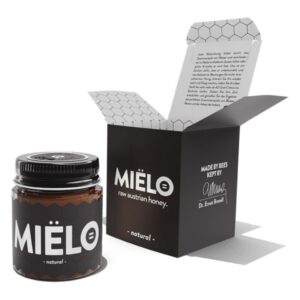 Ein Glas roher österreichischer Honig in einer schwarz-weißen Verpackung mit hexagonalem Muster und einer geöffneten Klappbox.